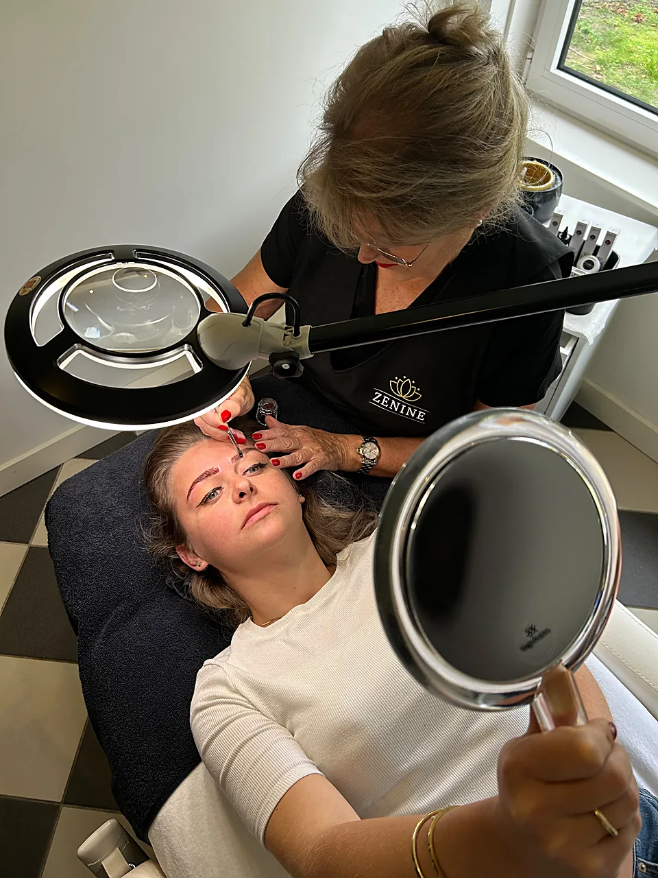 Ine Schrijver werkt de wenkbrauwen van een klant bij onder de loeplamp in salon Zenine