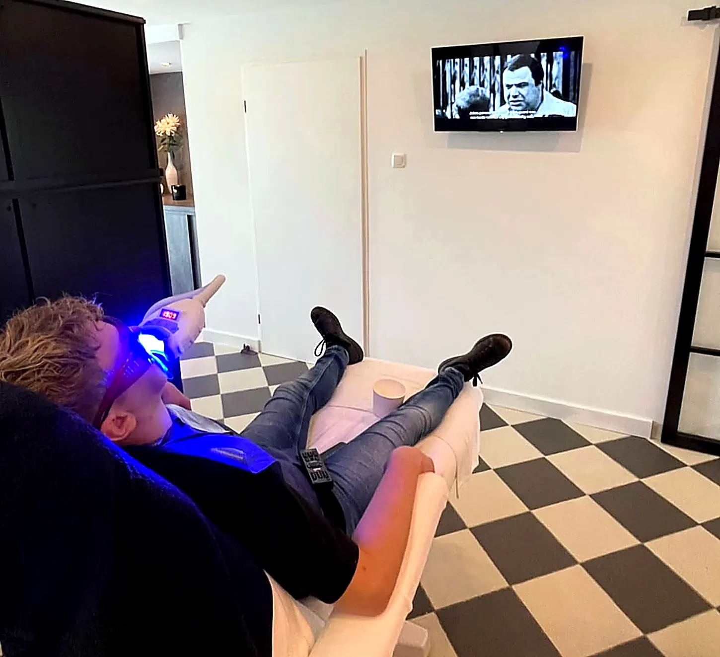 Klant ontspannen op de behandelstoel bij Zenine tijdens het tanden bleken met de blauwe ledlamp, met een film op de tv